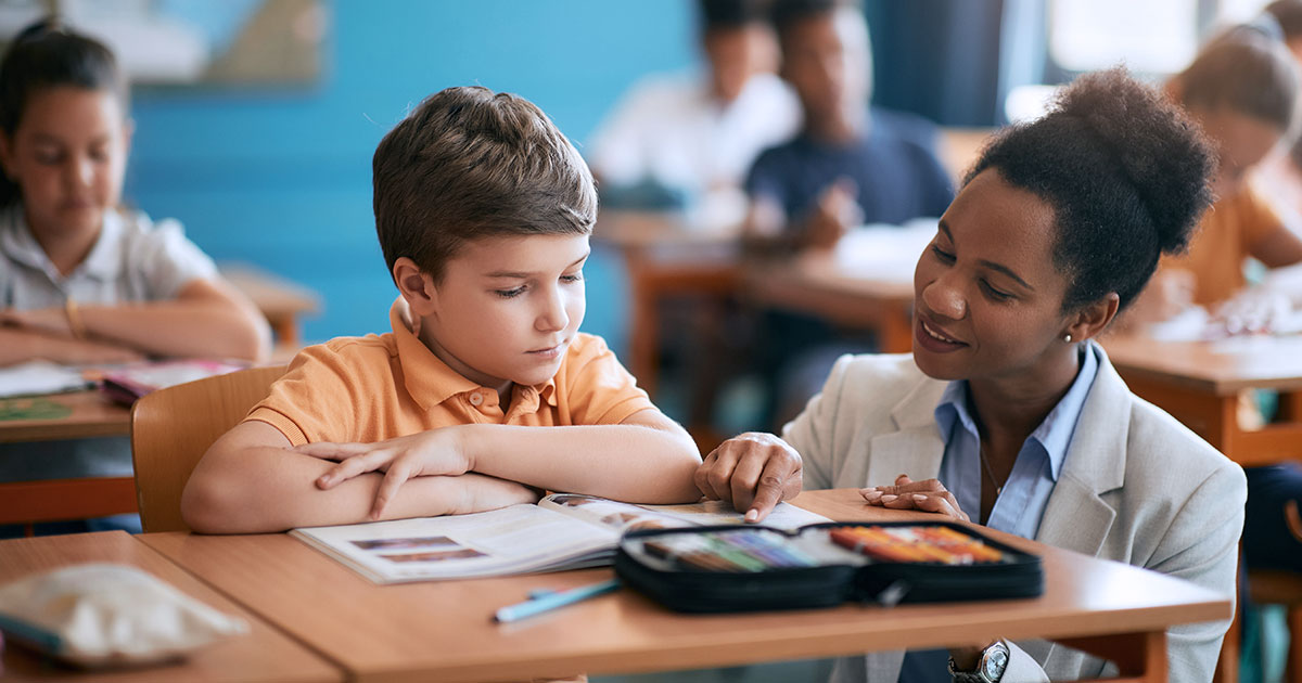 A teacher assisting a young student who sits at a desk