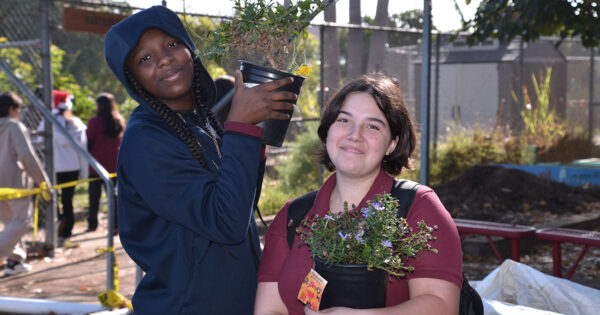 Two 8th grade students standing in a garden, each holding potted plants